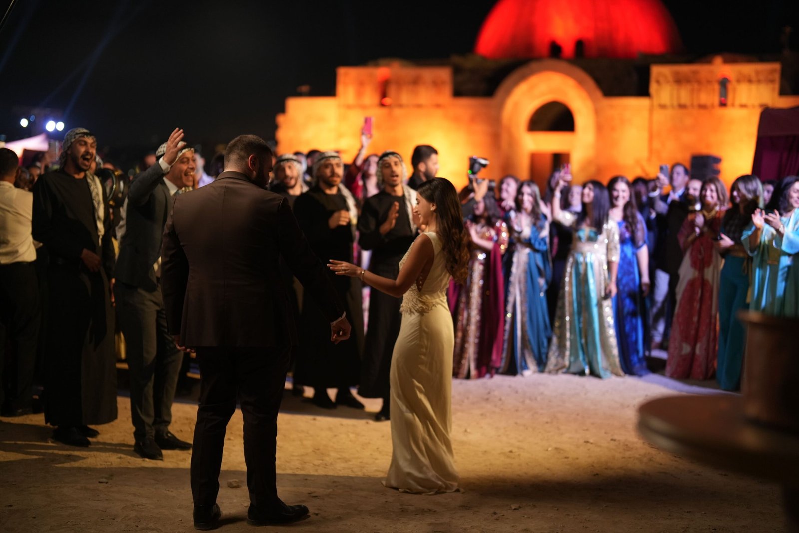 Guests and bride standing in front of orange-lit heritage façade at night